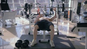 Bodybuilder training, strong muscular man bare-chested doing bench press with barbell while power working out in fitness