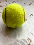 A bola de tênis macia amarela para jogar o tênis encontra-se em uma tabela no fundo de uma toalha de mesa branca fotografia de stock A bola de tênis macia amarela para jogar o tênis encontra-se em uma tabela no fundo de uma toalha de mesa branca fotografia de stock