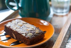 Bolo da brownie com a porca cortada na placa cerâmica alaranjada colocada na frente da caneca de café fotos de stock Bolo da brownie com a porca cortada na placa cerâmica alaranjada colocada na frente da caneca de café fotos de stock