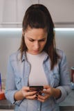 Boos meisje die mobiele telefoon in de keuken bekijken stock afbeelding Boos meisje die mobiele telefoon in de keuken bekijken stock afbeelding