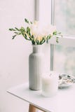 Bouquet of white freesias in vase and aromatic candle on table Royalty Free Stock Image Bouquet of white freesias in vase and aromatic candle on table Royalty Free Stock Image
