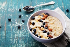 Bowl of fresh oatmeal porridge with banana, blueberries, almonds, coconut and caramel sauce on teal rustic table