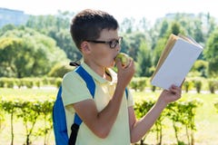 Boy eats an apple and reads an interesting book on his way home from school through the park royalty free stock photo Boy eats an apple and reads an interesting book on his way home from school through the park royalty free stock photo