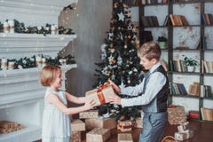 Boy and girl dressed elegantly standing in a bright room by the fireplace. Christmas tree in the background. New year concept. stock photo Boy and girl dressed elegantly standing in a bright room by the fireplace. Christmas tree in the background. New year concept. stock photo