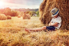 Boy leaning and sleeping against a haystack at sunset Stock Photo Boy leaning and sleeping against a haystack at sunset Stock Photo