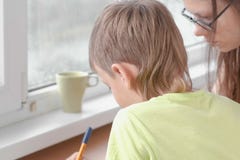 Boy learns to write letters sitting by the table. Doing homework with his mom. royalty free stock images Boy learns to write letters sitting by the table. Doing homework with his mom. royalty free stock images