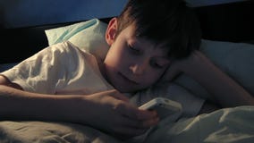 Boy resting in his bed in the evening and using his smart phone stock video Boy resting in his bed in the evening and using his smart phone stock video