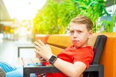 A boy with a smartphone sits on a bench and writes and reads a message and looks at the camera. Photo with tinting stock images A boy with a smartphone sits on a bench and writes and reads a message and looks at the camera. Photo with tinting stock images
