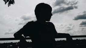 The boy stands on the waterfront against the sky. Silhouette of a boy.