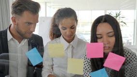 Brainstorming, workers looking at glass wall planner with notes in boardroom, young business team writing down ideas on stock video footage Brainstorming, workers looking at glass wall planner with notes in boardroom, young business team writing down ideas on stock video footage