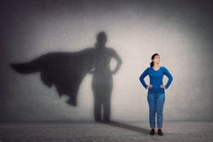 Brave woman keeps arms on hips, smiling confident, casting a superhero with cape shadow on the wall. Ambition and business success