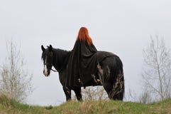 Brave woman with red hair in black cloak on friesian horse royalty free stock photos Brave woman with red hair in black cloak on friesian horse royalty free stock photos