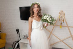 The bride in a beautiful wedding dress with a long curly hair stands in the bedroom and looks at the camera. Bride indoors with wh Stock Photos The bride in a beautiful wedding dress with a long curly hair stands in the bedroom and looks at the camera. Bride indoors with wh Stock Photos