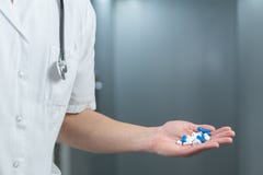 Bright close up of male doctor in uniform with stethoscope and holding blue and white pills in a hand royalty free stock photos Bright close up of male doctor in uniform with stethoscope and holding blue and white pills in a hand royalty free stock photos