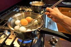 Brown eggs being removed from boiling water on gas stove