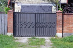 Brown metal gate with forged pattern and part of a brick fence outside stock photo Brown metal gate with forged pattern and part of a brick fence outside stock photo