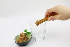 Brown sugar cubes on a blue plate woman hand hold a wooden tweezers a sugar cube in a glass cup on white background Stock Image Brown sugar cubes on a blue plate woman hand hold a wooden tweezers a sugar cube in a glass cup on white background Stock Image
