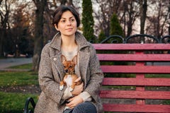 Brunette Girl Holds Small Toy Terrier Dog In Her Arms While Sitting On Red Bench In Autumn Park Stock Images
