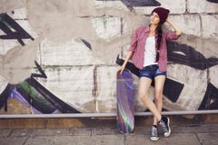 Brunettejugendliche in der Hippie-Ausstattung (kurze Jeanshose, keds, kariertes Hemd, Hut) mit einem Skateboard am Park lizenzfreies stockbild Brunettejugendliche in der Hippie-Ausstattung (kurze Jeanshose, keds, kariertes Hemd, Hut) mit einem Skateboard am Park lizenzfreies stockbild