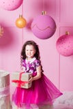 Brunettflickabarn 5 gamla år i en rosa klänning i rosa kvartsrum för ferie med gåvor royaltyfri foto Brunettflickabarn 5 gamla år i en rosa klänning i rosa kvartsrum för ferie med gåvor royaltyfri foto