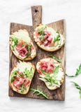 Bruschetta with cream cheese, pear, prosciutto and arugula on wooden chopping board on light background Royalty Free Stock Images Bruschetta with cream cheese, pear, prosciutto and arugula on wooden chopping board on light background Royalty Free Stock Images