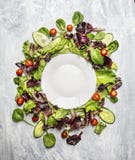 Bunter gesunder Salat mit Gurke und Tomaten um weiße leere Platte, auf hellgrauem hölzernem Hintergrund, Draufsicht Lizenzfreie Stockbilder Bunter gesunder Salat mit Gurke und Tomaten um weiße leere Platte, auf hellgrauem hölzernem Hintergrund, Draufsicht Lizenzfreie Stockbilder