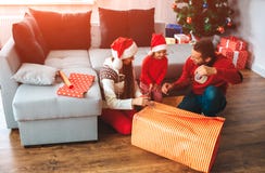 Buon Natale e buon anno La famiglia si siede sul pavimento vicino alla grande scatola del presente Il giovane mostra a sua figlia fotografia stock libera da diritti Buon Natale e buon anno La famiglia si siede sul pavimento vicino alla grande scatola del presente Il giovane mostra a sua figlia fotografia stock libera da diritti