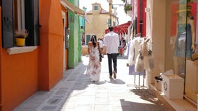 Couple in love walking holding hands along colored shop windows on street. Burano, Italy 19 May 2018: tourists at europe, couple in love walking holding hands Couple in love walking holding hands along colored shop windows on street. Burano, Italy 19 May 2018: tourists at europe, couple in love walking holding hands