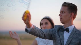 Burbujas de la risa hermosa de novia y del novio y de jabón del soplo en el parque en la puesta del sol almacen de metraje de vídeo Burbujas de la risa hermosa de novia y del novio y de jabón del soplo en el parque en la puesta del sol almacen de metraje de vídeo