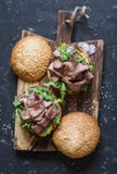Burger μπριζόλας βόειου κρέατος με τα τουρσιά, mayo τη σάλτσα, το arugula και το κόκκινο κρεμμύδι σε έναν αγροτικό ξύλινο τέμνοντ Στοκ Φωτογραφία Burger μπριζόλας βόειου κρέατος με τα τουρσιά, mayo τη σάλτσα, το arugula και το κόκκινο κρεμμύδι σε έναν αγροτικό ξύλινο τέμνοντ Στοκ Φωτογραφία