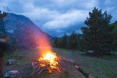 Burning camp fire into remote larch and pine tree woodland with high altitude landscape and dramatic sky at dusk. Summer adventure Stock Photos Burning camp fire into remote larch and pine tree woodland with high altitude landscape and dramatic sky at dusk. Summer adventure Stock Photos
