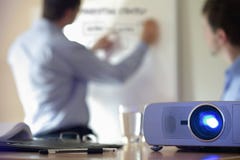 Presentation with lcd projector. Business conference or lecture with businessman writing on whiteboard and lcd projector in foreground Presentation with lcd projector. Business conference or lecture with businessman writing on whiteboard and lcd projector in foreground