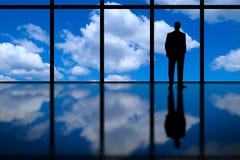 Business Man Looking Out of High Rise Office Window at Blue Sky and Clouds