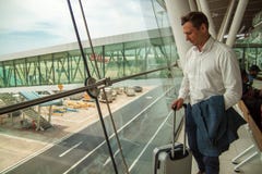 Young handsome businessman is standing with a suitcase near the window at the airport, waiting for his flight. royalty free stock photos Young handsome businessman is standing with a suitcase near the window at the airport, waiting for his flight. royalty free stock photos