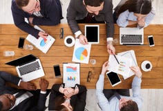 Business meeting top view. Multiethnic emploees listen to the report in office, top view of wooden table Stock Photo Business meeting top view. Multiethnic emploees listen to the report in office, top view of wooden table Stock Photo