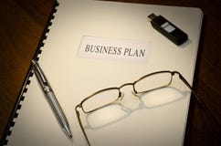 Business Plan. On a desk wiht a pen, a thumb drive and a pair of glasses Business Plan. On a desk wiht a pen, a thumb drive and a pair of glasses
