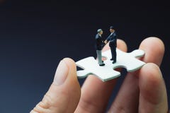 Business success strategy with collaboration, teamwork or negotiation jigsaw key, miniature people businessmen handshaking on