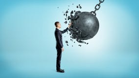 A businessman on blue background touching a wrecking ball when it crashes under his hand. Stock Photography A businessman on blue background touching a wrecking ball when it crashes under his hand. Stock Photography