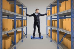 A businessman stands on a self-balancing scooter between two full storage racks. stock photography A businessman stands on a self-balancing scooter between two full storage racks. stock photography