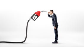 A businessman on white background staring closely at a large red gas nozzle attached to a black hose. Stock Photos A businessman on white background staring closely at a large red gas nozzle attached to a black hose. Stock Photos