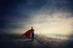 Businesswoman as confident superhero with red cape stands on the rooftop looking over city horizon. Ambition and business success
