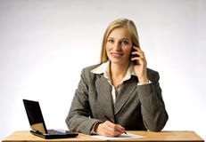 Businesswoman with gray jacket sitting at office tesk, talking on phone and writing a note with a pen on a paper. royalty free stock photo Businesswoman with gray jacket sitting at office tesk, talking on phone and writing a note with a pen on a paper. royalty free stock photo