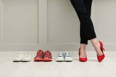 Businesswoman in high heel shoes standing near different comfortable sneakers indoors, closeup