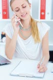 Young Caucasian businesswoman talking on the phone and writing notes in office. Focus on document. stock images Young Caucasian businesswoman talking on the phone and writing notes in office. Focus on document. stock images