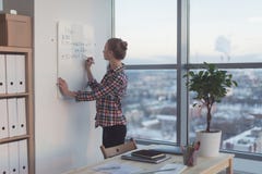 Businesswoman writing day plan on white magnet board, modern office. Side view of caucasian female employee planning stock image Businesswoman writing day plan on white magnet board, modern office. Side view of caucasian female employee planning stock image