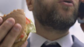 Busy businessman talking on phone and eating burger, unhealthy fast food