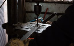 Byggnadsarbetaren borrar hålet i stång av metalljärn genom att använda den industriella drillborren royaltyfri fotografi Byggnadsarbetaren borrar hålet i stång av metalljärn genom att använda den industriella drillborren royaltyfri fotografi