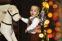 Bébé heureux mignon près de cheval de basculage dans une salle décorée de Noël avec le bokeh photographie stock Bébé heureux mignon près de cheval de basculage dans une salle décorée de Noël avec le bokeh photographie stock