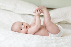 Bébé mignon se trouvant sur la feuille blanche et tenant ses jambes Image stock Bébé mignon se trouvant sur la feuille blanche et tenant ses jambes Image stock