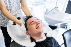 Cabeleireiro do homem que limpa a cabeça de um cliente de sorriso considerável com uma toalha no barbeiro imagem de stock Cabeleireiro do homem que limpa a cabeça de um cliente de sorriso considerável com uma toalha no barbeiro imagem de stock